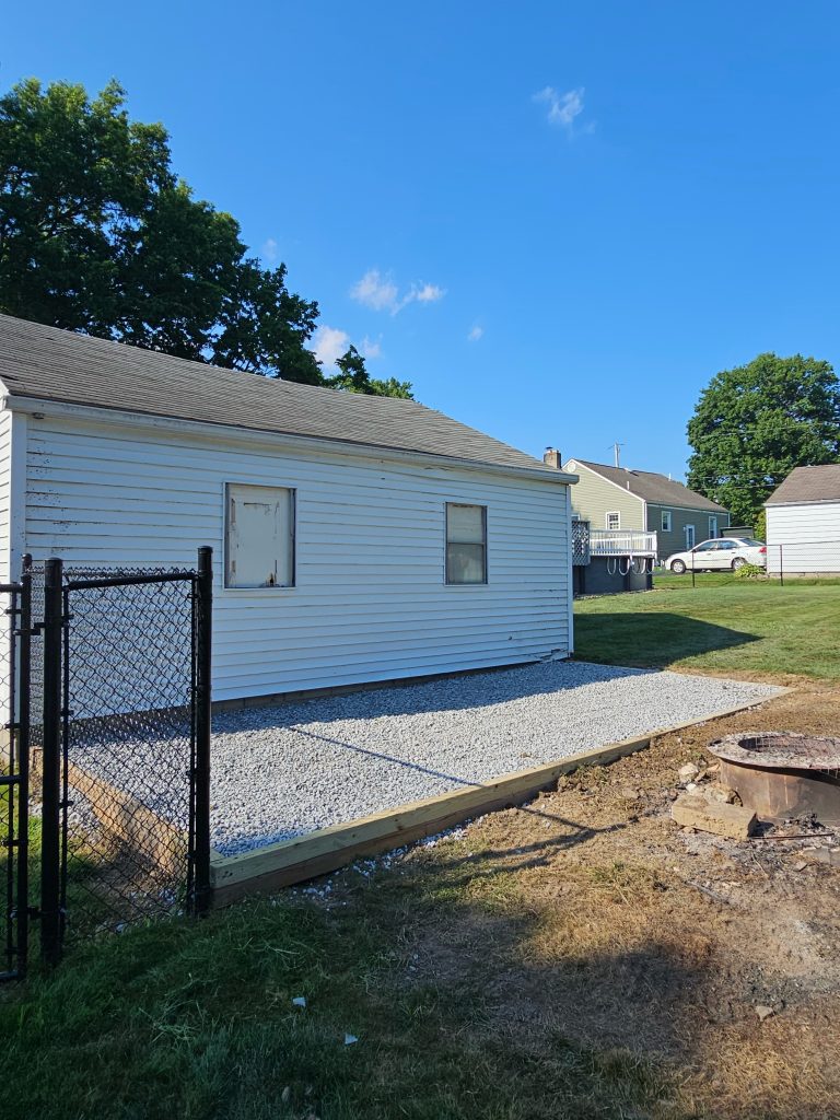Shed pad with gravel right beside another building.